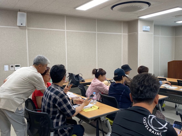 우리마을 사진 달인을 찾아라!기획홍보분과 사진달인을 찾아라 강의에서 강사가 수강생들의 핸드폰을 바라보며 지도 하고 있는 모습