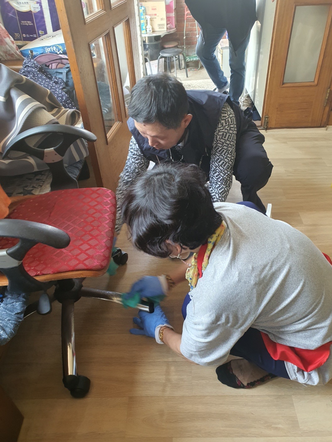 치매예방을 위한 원예치료 및 정리수납 봉사독거노인을 위한 정리수납 봉사에서 봉사자가 오래된 의자의 다리부분을 걸레로 닦아주고 있는 모습