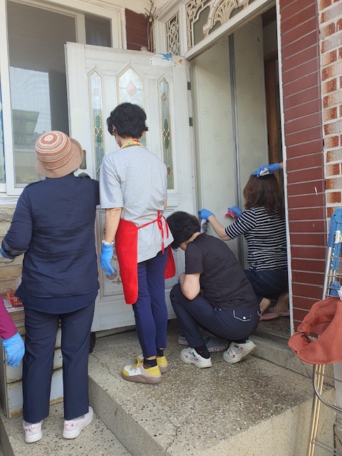 치매예방을 위한 원예치료 및 정리수납 봉사독거노인을 위한 정리수납 봉사에서 봉사자들이 주택 현관문을 청소해주고 있는모습