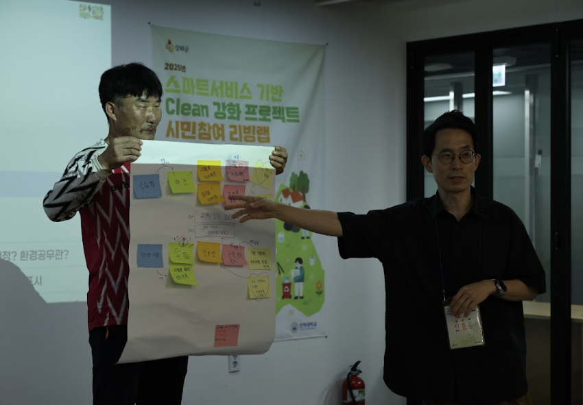 포스트잇이 붙여진 종이를 든 남성과 또다른 남성이 손으로 가리키며 발표하고 있는 모습