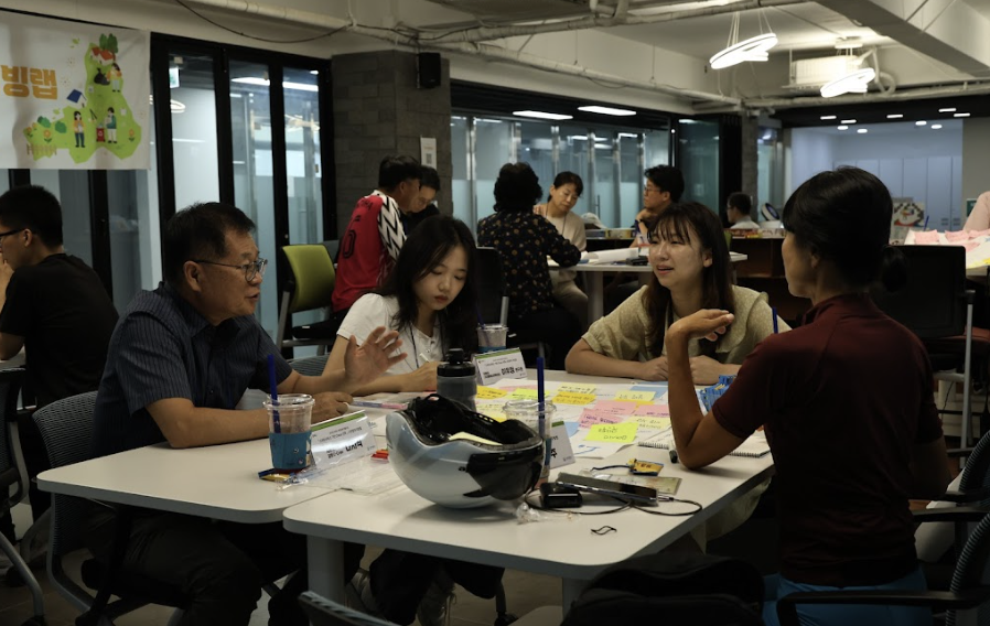 3명의 젊은 여성 참석자와 중년 남성 한명이 서로 대화를 나누고 메모를 하고 있는 모습