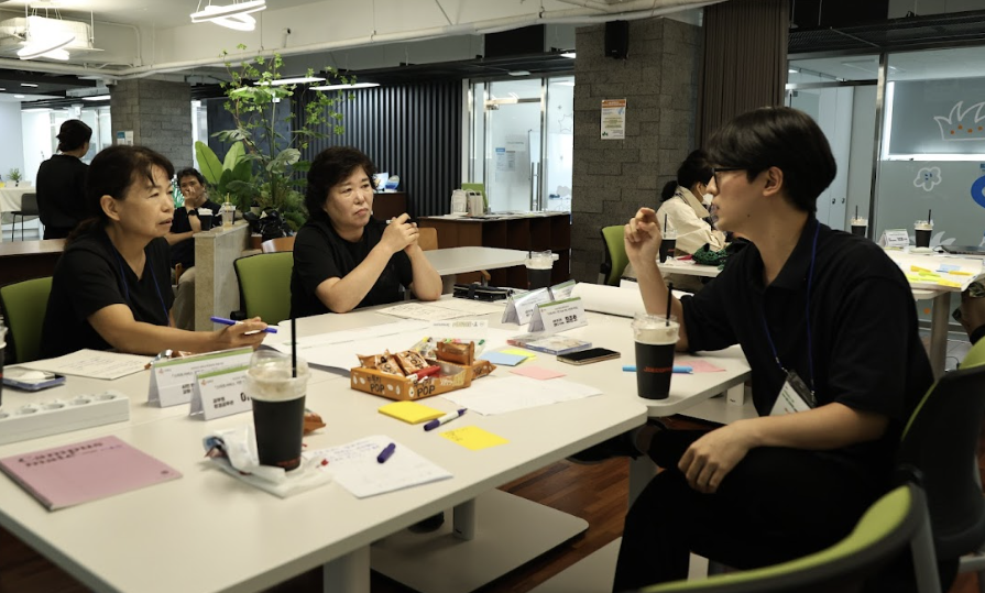 중년의 한 여성 참가자가 종이를 들고 다른 사람들에게 말하는 모습